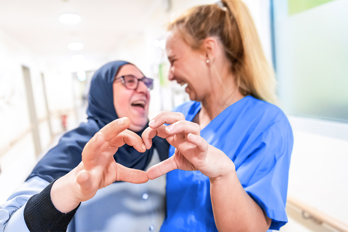 Bewohnerin und Pflegerin formen ein gemeinsames Herz mit ihren Händen